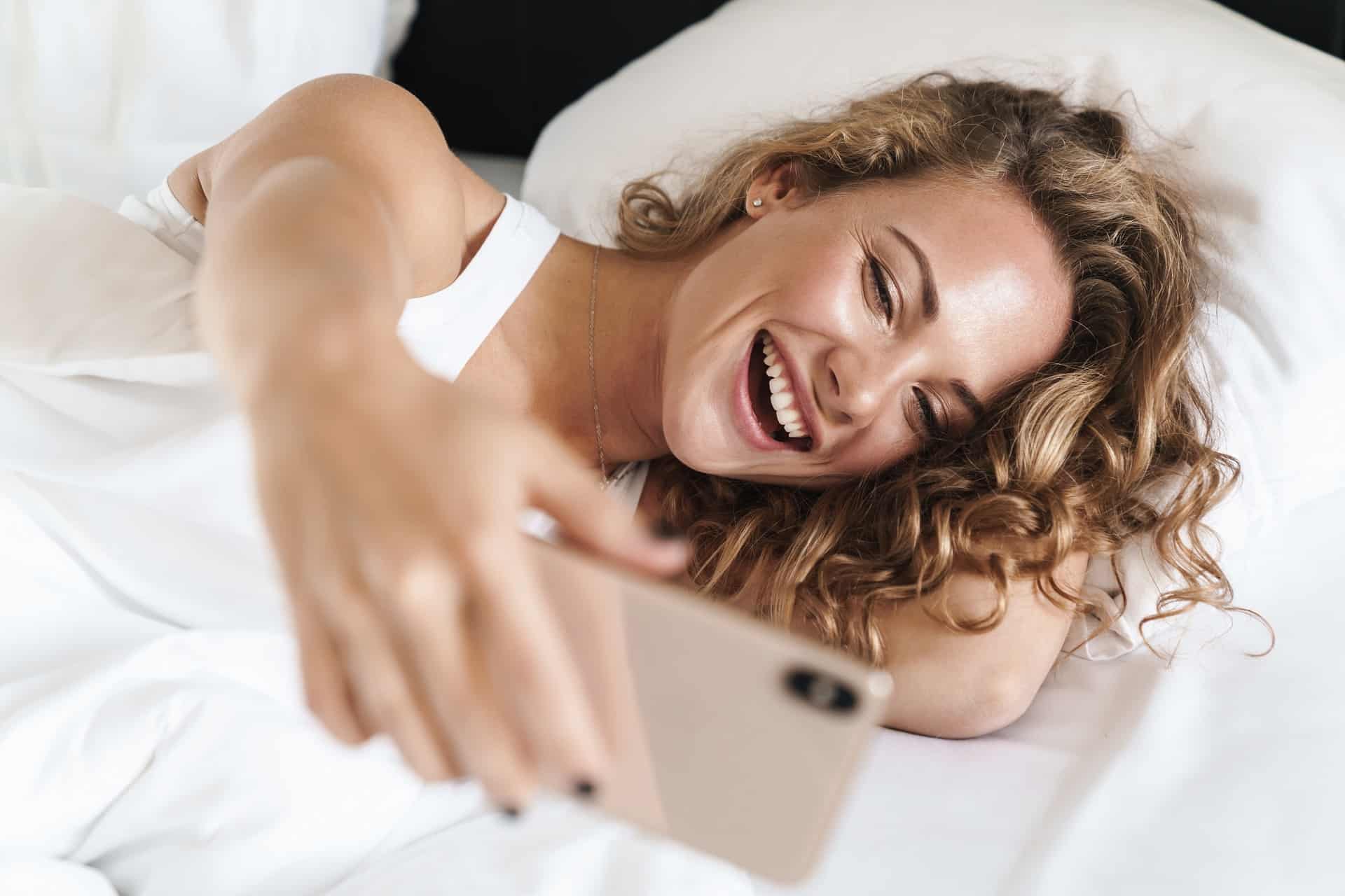 Жена с телефон си прави селфи в леглото