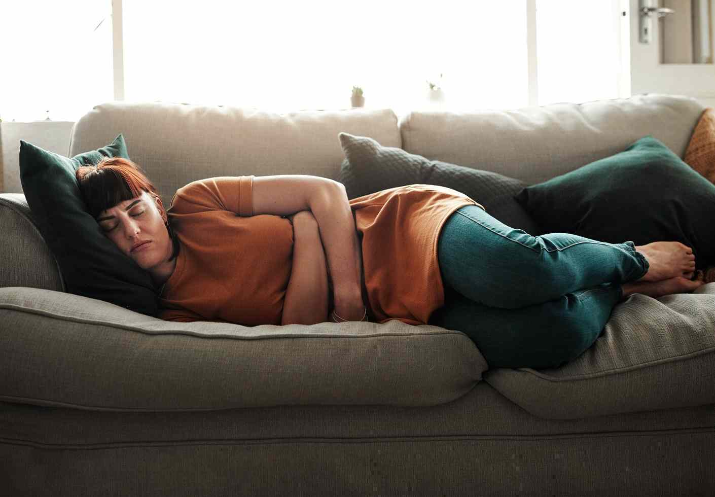 Жена лежаща на диван с болки в корема