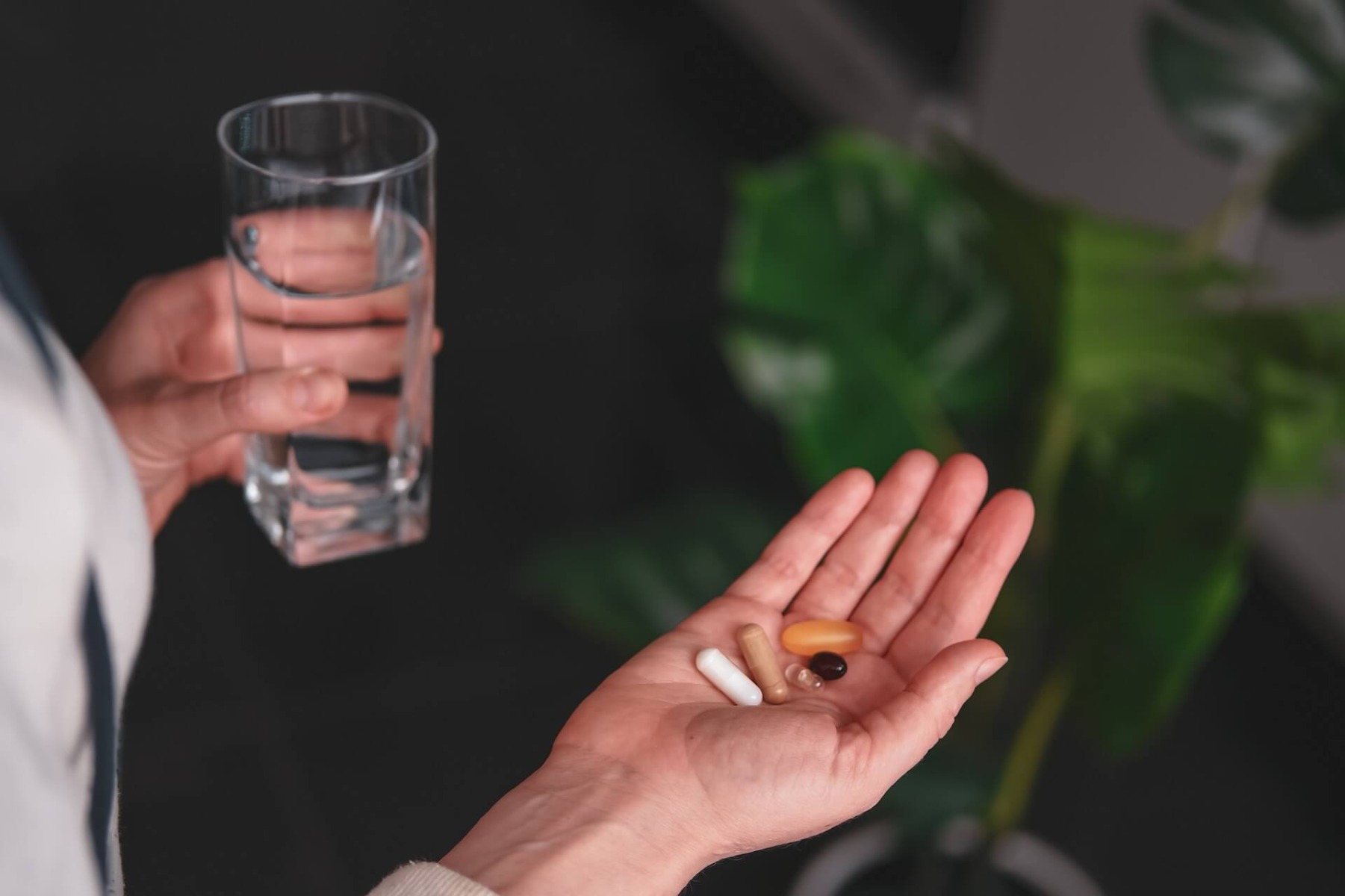 човек държащ чаша с вода в едната и таблетки с другата ръка