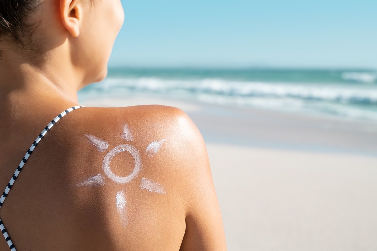 Жена на плаж. На гърба и има нарисувано слънце със слънцезащитен крем